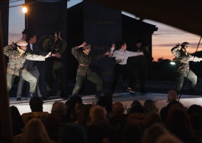 The cast are on stage, jumping around, smiling and doing a final dance as the performance is finished