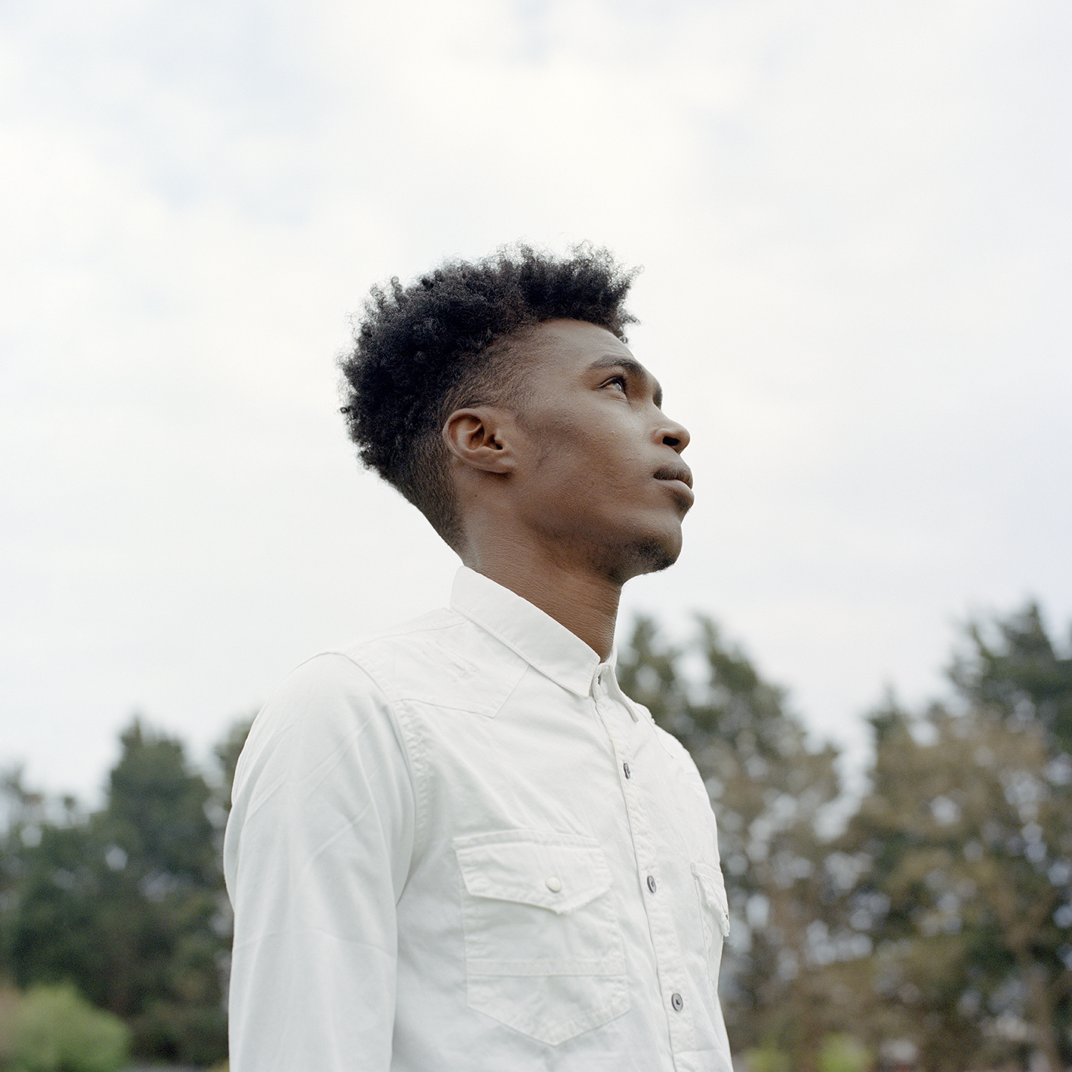 A man looking into the distance, he is wearing a white shirt.