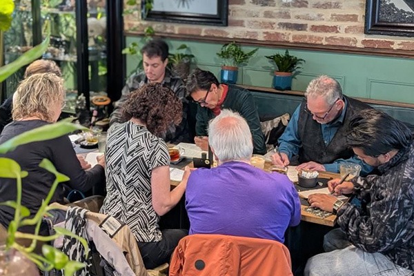 Group of people, gathered around a table. All writing and concentrating on their work.